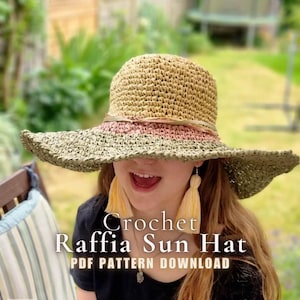 May include: A crochet raffia sun hat featuring a tan crown and a wide, olive green brim with a thin pink band around the base. The text Crochet Raffia Sun Hat PDF PATTERN DOWNLOAD is overlaid on the image. The hat is paired with long yellow tassel earrings.
