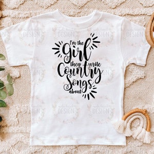 Puede incluir: Camiseta blanca con texto negro que dice "Soy la chica de la que escriben canciones country".