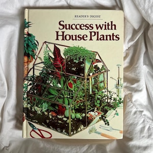 May include: A vintage book titled "Success with House Plants" by Reader's Digest. The cover features a terrarium with various green plants and red accents. Gardening tools and a watering can are also visible.