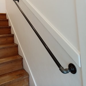Peut inclure: Rampe d'escalier en métal noir avec deux brides en métal noir fixées à un mur blanc. La rampe est montée sur un mur blanc avec une moulure blanche.