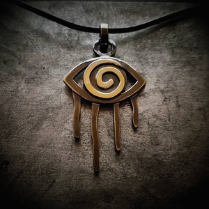 Op de afbeelding: Een zilveren oog kettinghanger met een gouden spiraalvormig ontwerp en hangende druppelvormen.