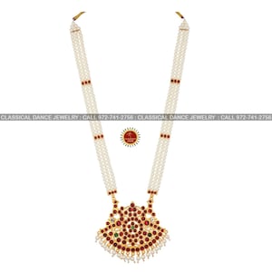 May include: A traditional Indian necklace with a gold pendant adorned with red and green gemstones. The necklace is made of white pearls and has a three-strand design.