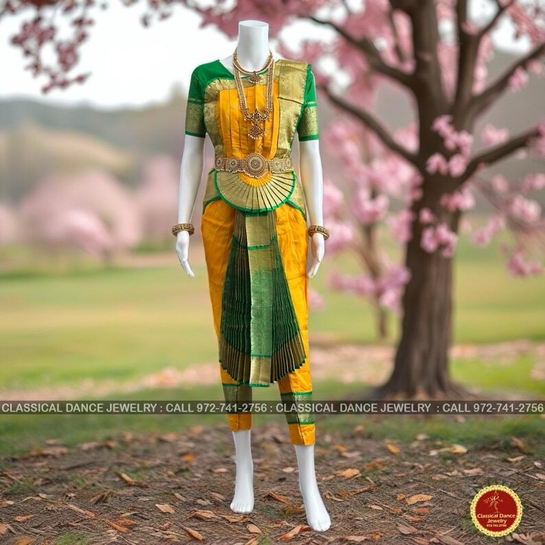 May include: A yellow and green classical dance costume on a mannequin. The costume features a gold-colored necklace, belt, and armbands. The outfit includes a yellow top with green sleeves, yellow pants, and a green and gold skirt. The background is a blurred outdoor scene.
