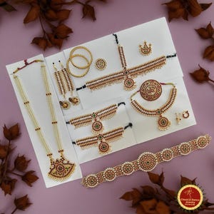 May include: An assortment of classical dance jewelry, including necklaces, earrings, bracelets, and headpieces. The jewelry features red, green, and white accents, with a gold-colored metal base. The pieces are arranged on white cards against a purple background.