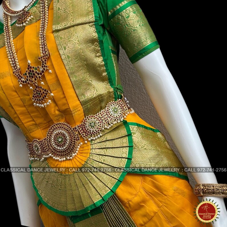 May include: A traditional Indian dance costume in yellow and green, featuring ornate gold jewelry with red and green accents. The costume includes a necklace, waist belt, and arm cuffs. The image also includes the text "CLASSICAL DANCE JEWELRY".
