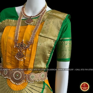May include: A mannequin displays a traditional Indian dance costume. The ensemble features a yellow and green sari with gold accents, and ornate jewelry. The jewelry includes a necklace, long pendant, and a waist belt, all adorned with red and green stones.