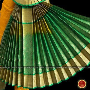 May include: Close-up of a green and gold traditional dance costume. The fabric is pleated and has gold trim. The costume is likely for classical Indian dance. The image includes the text "CLASSICAL DANCE JEWELRY: CALL 972-741-2756".