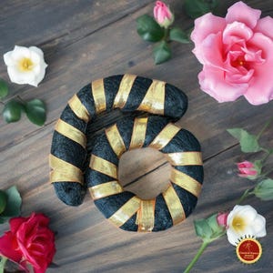May include: A decorative number six made of black material wrapped with gold ribbon. The number is surrounded by pink and white roses and green leaves, set against a wooden background.