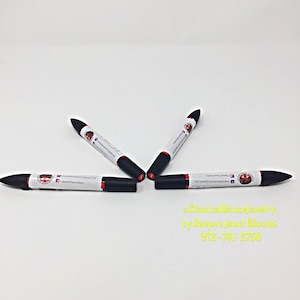 May include: Four black and red dual-tip markers on a white background. Each marker features a white label with text and a logo. The image also includes yellow text: "ClassicalDanceJewelry by Deepa's Jewel Blooms".