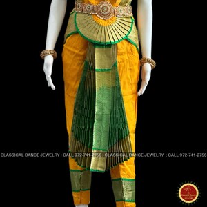 May include: A yellow and green classical dance costume with gold accents. The costume features a pleated green skirt, a gold belt with intricate detailing, and gold trim. The costume is displayed on a mannequin. The text "CLASSICAL DANCE JEWELRY" is visible.