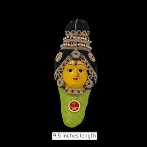May include: A traditional Indian headpiece with a yellow face, black hair, and elaborate gold and jewel-toned decorations. The headpiece is 9.5 inches long and is made of fabric and beads.