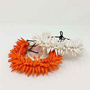 May include: Two floral hair ornaments, one orange and one white, made of paper flowers. The ornaments are arranged on a white background. The text "Classical Dance Jewelry" is visible in the image.