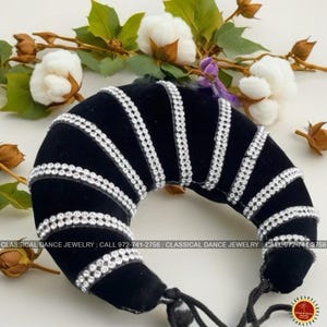 Peut inclure: Un accessoire de cheveux en velours noir, en forme de croissant, orné de rangées de strass étincelants. L'accessoire est pour les bijoux de danse classique. Le texte "CLASSICAL DANCE JEWELRY" et un numéro de téléphone sont visibles.