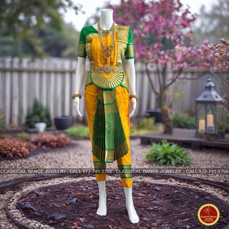 May include: A mannequin displays a traditional Indian classical dance costume. The ensemble features a yellow top and pants with green and gold accents. Gold jewelry and a decorative belt complete the look. The costume is designed for classical dance performances.
