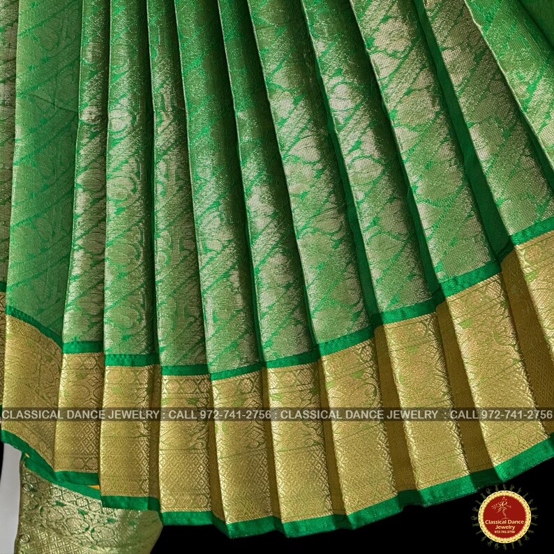 May include: Close-up of a green fabric with gold trim. The fabric has a textured pattern and is folded in vertical pleats. The bottom edge features a gold border with a green trim. The text "CLASSICAL DANCE JEWELRY" is visible.