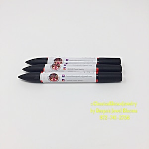 May include: Three black markers with red and white labels, arranged horizontally. Each label displays the text "Classical Dance Jewelry" and contact information. The background is plain white.