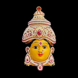 May include: A golden face sculpture of a woman with a jeweled crown and elaborate jewellery. The sculpture has a yellow face, red lips, and black eyes. The crown is adorned with red and white gems.