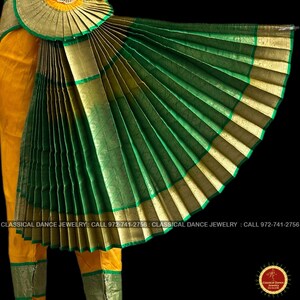 May include: A close-up of a traditional Indian classical dance costume. The costume features a fan-like green skirt with gold trim and a matching headpiece. The dancer is also wearing yellow pants with green trim.