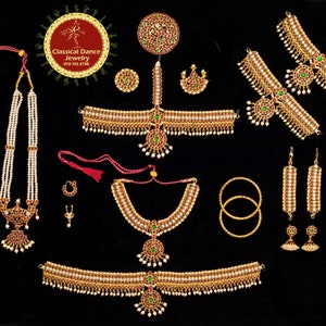 May include: A set of traditional Indian jewelry for dance performances, featuring a gold necklace with a green and red pendant, a matching headpiece, earrings, bangles, and a waist chain. The jewelry is decorated with pearls and red and green gemstones.