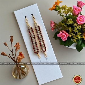 May include: Gold-toned jewelry with red and clear gemstones, displayed on a white card. The jewelry is designed for classical dance. The image also includes a vase of flowers and text that reads "CLASSICAL DANCE JEWELRY: CALL 972-741-2756".