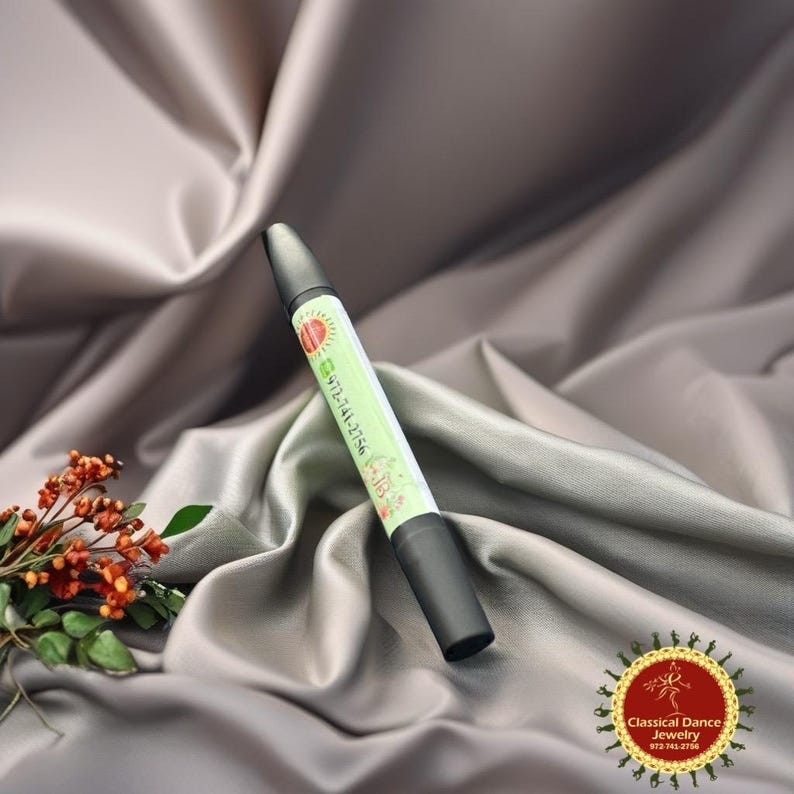 May include: A black and green pen with the text "972-741-2756" and a sun graphic. The pen is set against a backdrop of grey fabric and a small floral arrangement. The pen has a black tip and a black cap.