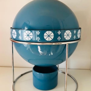 May include: A vintage teal-colored serving dish with a spherical design. It features a white floral pattern band and a chrome metal stand. The dish includes a lid and a base, perfect for keeping food warm.