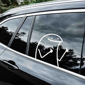 May include: A black car with a white sticker of a smiling cartoon character giving a thumbs up with both hands on the back window.