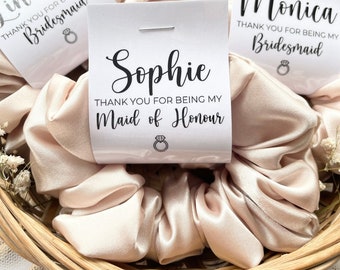 May include: A set of six hair scrunchies with personalized thank you cards for bridesmaids and maid of honor. The cards are white with black text and a small ring icon. The scrunchies are a light peach color.