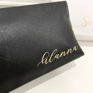 K&ouml;nnte beinhalten: Schwarze Kosmetiktasche aus Leder mit dem Namen "Alanna" in goldenen Lettern.
