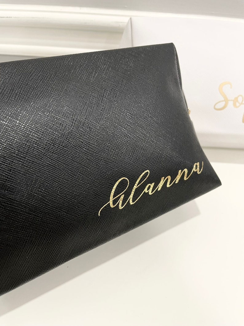 K&ouml;nnte beinhalten: Schwarze Kosmetiktasche aus Leder mit dem Namen "Alanna" in goldenen Lettern.