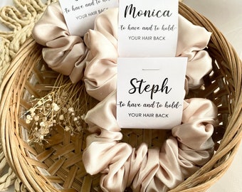 May include: Three satin scrunchies in a wicker basket with tags that read "Jess to have and to hold your hair back", "Monica to have and to hold your hair back", and "Steph to have and to hold your hair back".