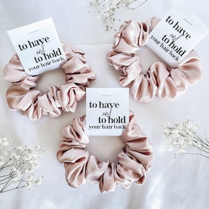 May include: Three pink satin scrunchies with white tags that say "to have and to hold your hair back".