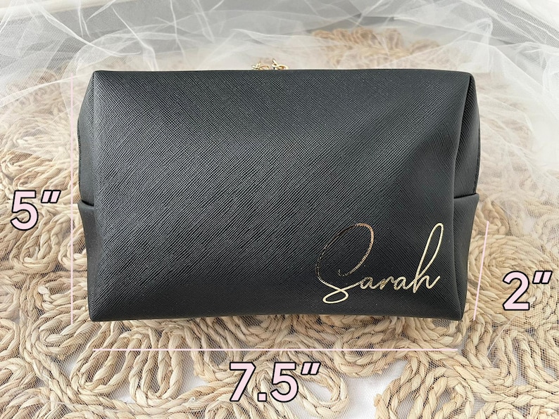 K&ouml;nnte beinhalten: Schwarze, gezippte Kosmetiktasche mit goldener Aufschrift "Sarah". Die Tasche misst 19 cm in der Breite, 13 cm in der H&ouml;he und 5 cm in der Tiefe.
