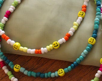Puede incluir: Tres collares de cuentas coloridas con dijes de caritas sonrientes. Los collares están hechos con cuentas turquesa, blancas, naranjas, rosas y verdes.