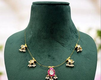 May include: A gold necklace with a pink and white stone pendant and three smaller pendants with white stones. The necklace is on a green velvet background.