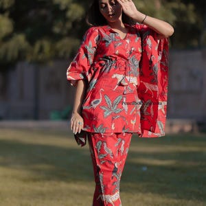 May include: Red two-piece pajama set with a tropical print featuring leopards, birds, and palm leaves. The set includes a short-sleeved top with a drawstring waist and matching trousers. The outfit is made of a lightweight fabric.