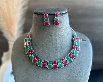 May include: A silver necklace with green and pink square-shaped stones. Matching earrings with the same stones are also included.