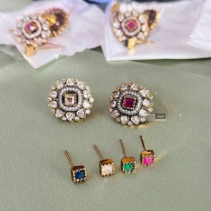 May include: A set of six gold-tone earrings with a floral design and a single stone in the center. The stones are red, green, blue, and clear.