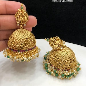 Könnte beinhalten: Ein Paar goldfarbene Ohrringe mit filigranen Designs und einem Pfauenmotiv. Die Ohrringe sind mit grünen und roten Steinen und weißen Perlen verziert.