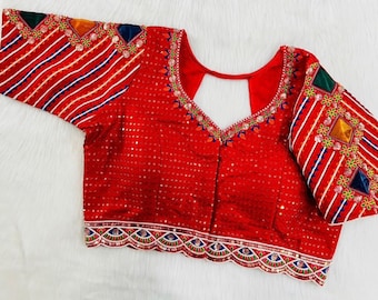 May include: A red embroidered blouse with a keyhole neckline and short sleeves. The blouse features intricate floral and geometric patterns in shades of blue, green, and gold.