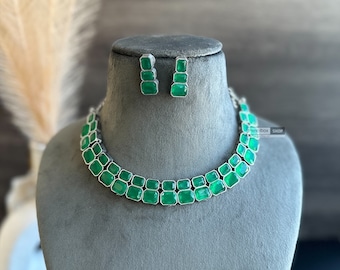 May include: A silver necklace and earrings set with green gemstone accents. The necklace features a double row of square-shaped stones.