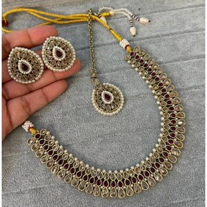 May include: A gold necklace with a layered design of white and burgundy stones. The necklace comes with matching earrings and a pendant.