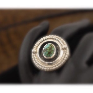 May include: A silver ring with a turquoise stone set in a circular bezel. The ring has a beaded design around the bezel.