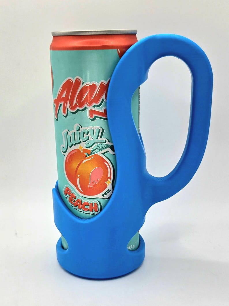 Op de afbeelding: Een blauwe blikjeshouder met een handvat, met een blikje Alani Nu Juicy Peach-frisdrank. Het blikje heeft een turquoise achtergrond met perzikafbeeldingen en rode en witte tekst. De houder is gemaakt van flexibel materiaal.