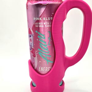 Op de afbeelding: Een roze blikje Alani Nu Energy drink in een bijpassende roze houder. Het blikje is voorzien van het opschrift "Pink Slush" en heeft een aardbei- en ijsje-afbeelding. De houder heeft een handvat.