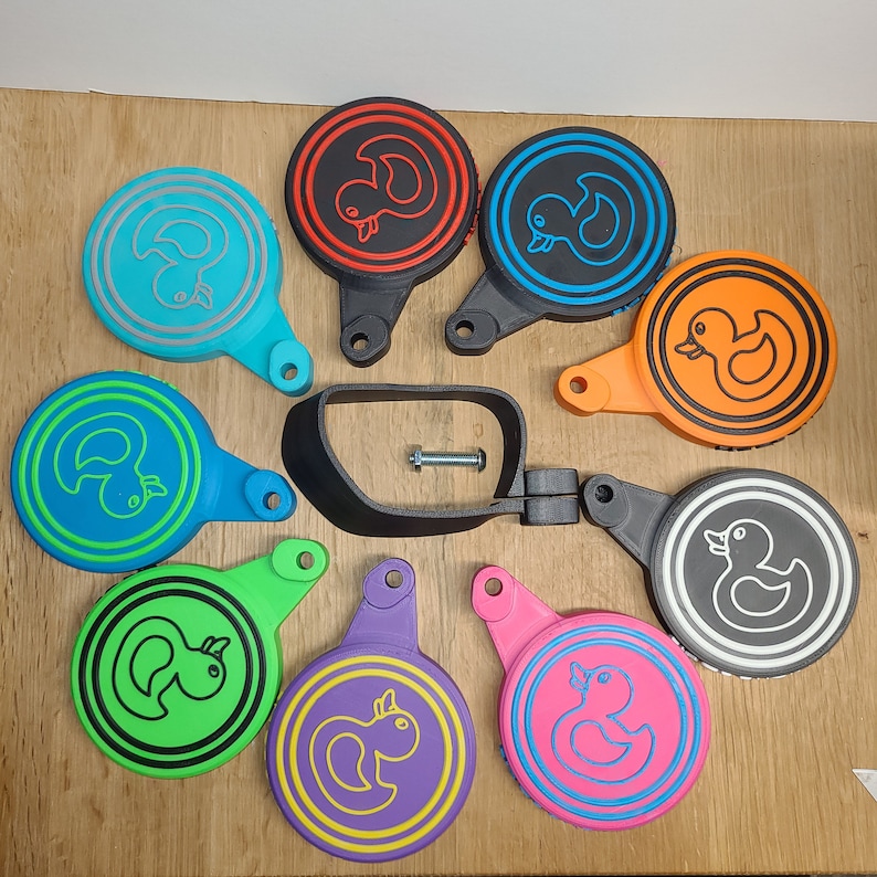May include: A set of nine colorful round rubber ducky keychains with different colored backgrounds and black outlines. The keychains are attached to a black metal bar with a screw.