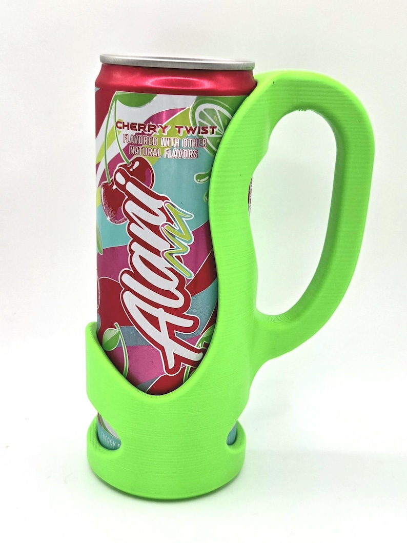 Op de afbeelding: Een felgroene blikhouder met een handvat, ontworpen om een blikje Alani Cherry Twist-frisdrank vast te houden. Het blikje is rood met een kleurrijk etiket met kersen en de merknaam. De houder biedt een stevige grip.