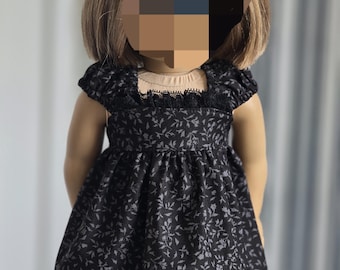 May include: A black doll dress with a floral pattern. The dress features short sleeves, a square neckline with lace trim, and a gathered skirt. The doll has blonde hair.