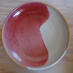 以下が含まれることがあります： ユニークなデザインの手作りセラミックプレート。プレートは、片側に鮮やかな赤ピンク色、もう片側にクリーミーな白というハーフ＆ハーフの配色です。縁は自然な、釉薬のかかっていない仕上がりです。食べ物を出すのに最適です。