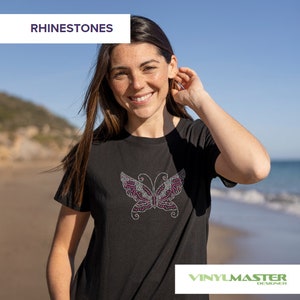 Puede incluir: Una camiseta negra con un dise&ntilde;o de mariposa de brillantes de color rosa. La camiseta la lleva puesta una persona en una playa. El texto "RHINESTONES" est&aacute; en la esquina superior izquierda de la imagen. El texto "VINYLMASTER DESIGNER" est&aacute; en la esquina inferior derecha de la imagen.